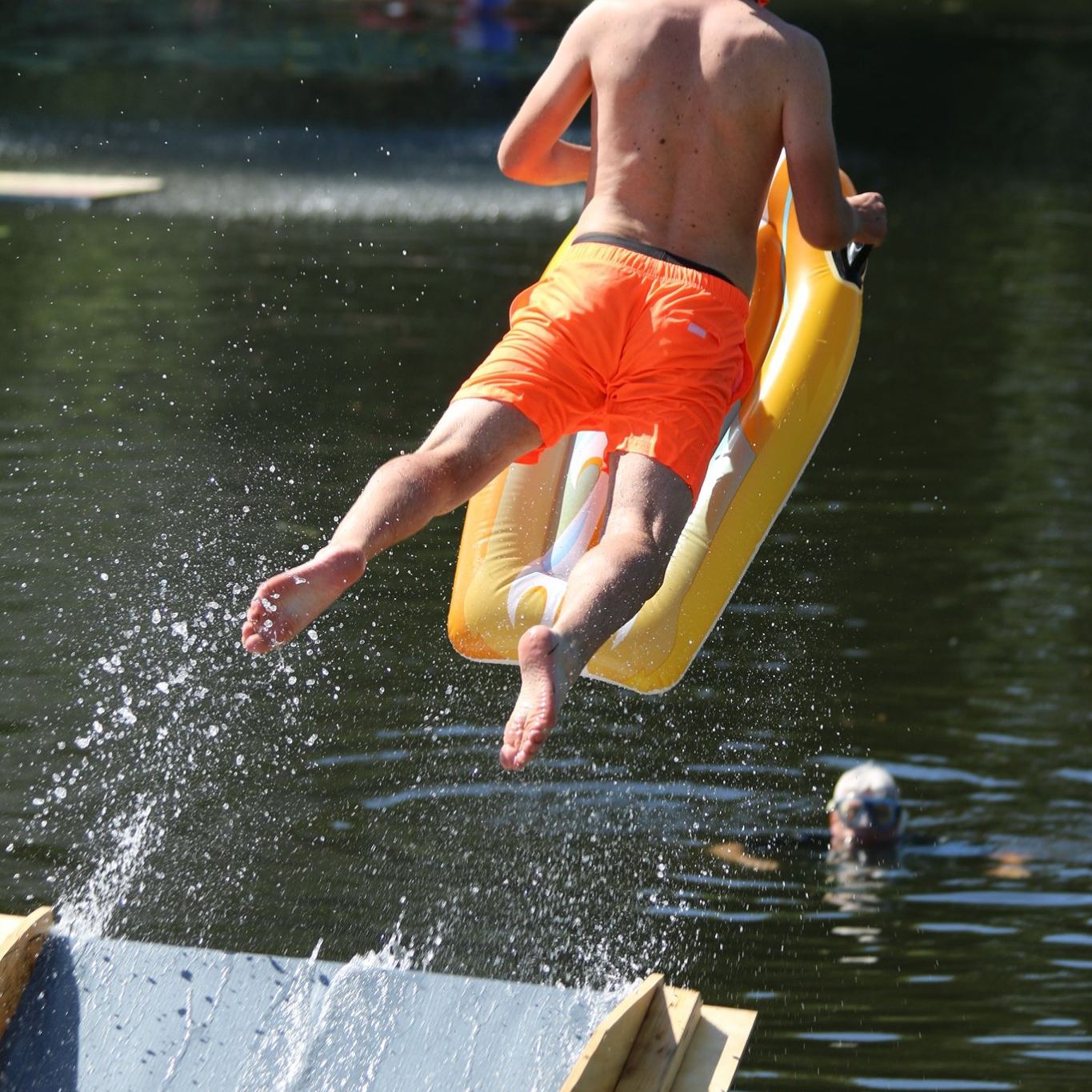 Een deelnemer springt met een opblaasbaar zwembandje het water in